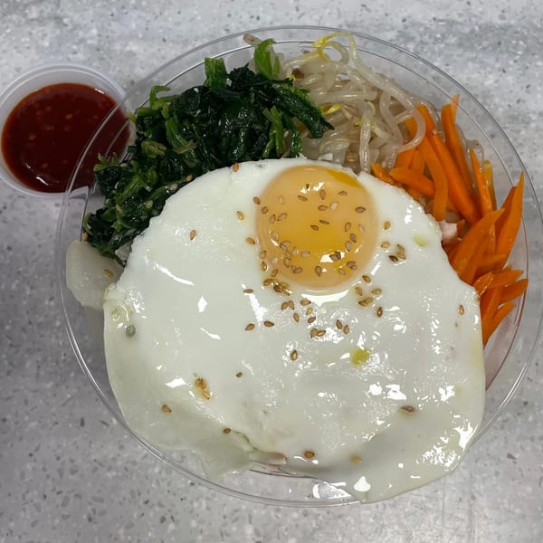 Bibimbap from Sue's Kimbap House with a fried egg, spinach, bean sprouts, and carrots, with sauce on the side.