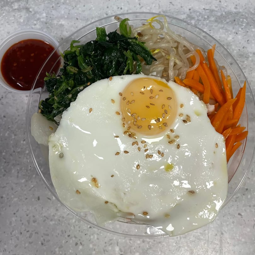 Bibimbap from Sue's Kimbap House with a fried egg, spinach, bean sprouts, and carrots, with sauce on the side.