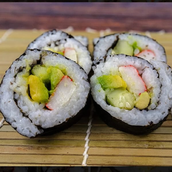 Four pieces of Sue's Kimbap, filled with avocado, cucumber, and crab meat, on a bamboo mat.