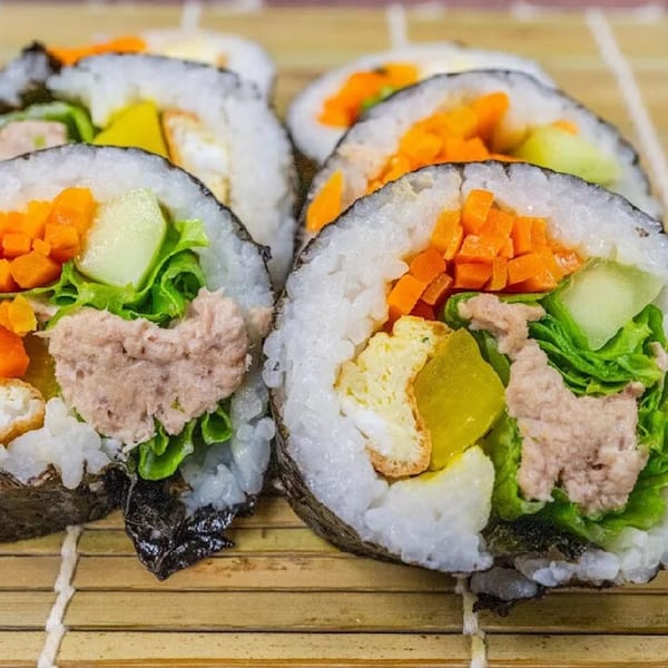 Close-up of several Sue's Kimbap House tuna kimbap rolls with various fillings on a bamboo mat.
