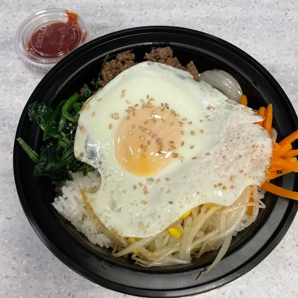 Bibimbap with a fried egg, ground meat, spinach, carrots, bean sprouts, and sauce on the side.
