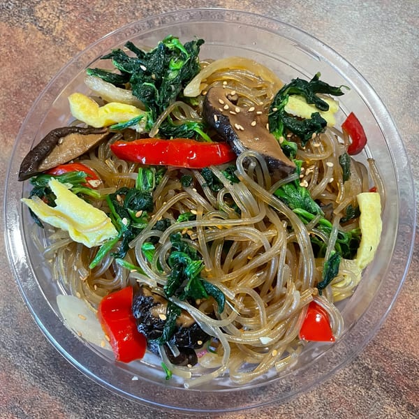 Korean japchae noodles with spinach, mushrooms, red peppers, and egg in a clear bowl.