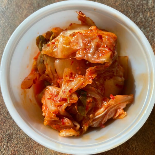 A white bowl filled with vibrant red kimchi, a traditional Korean side dish from Sue's Kimbap House.